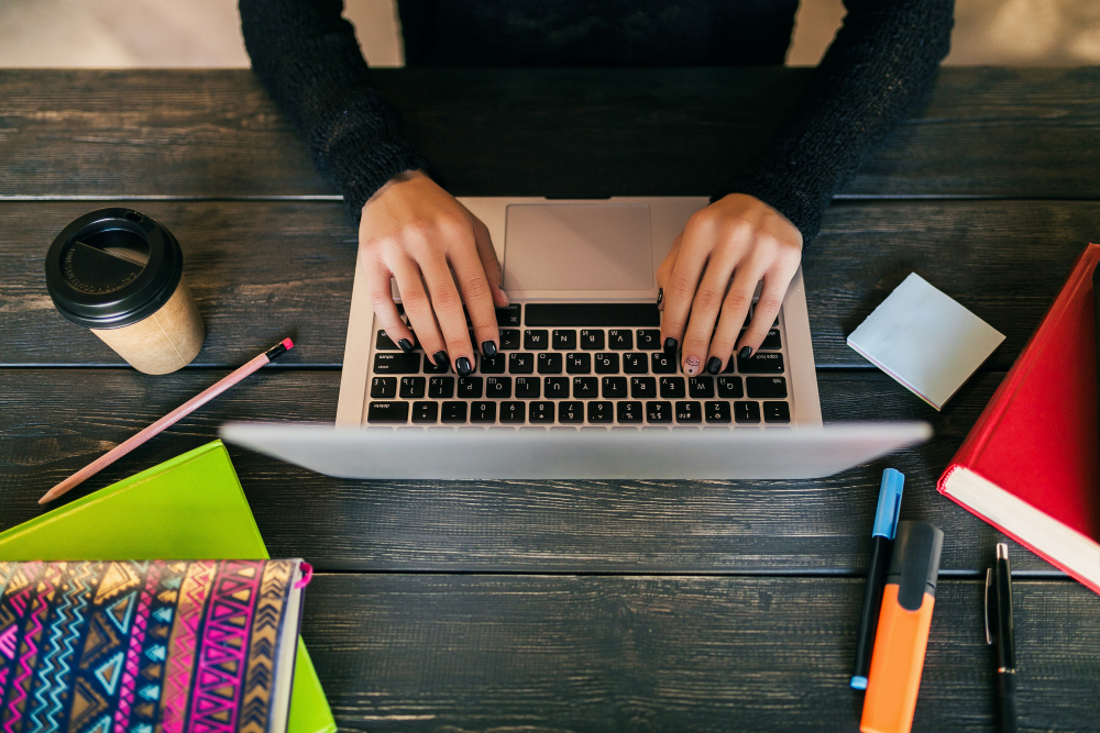 view-from-hands-pretty-woman-sitting-table-black-shirt-working-laptop-co-working-office-stationery-hands-typing-drinking-coffee-freelance